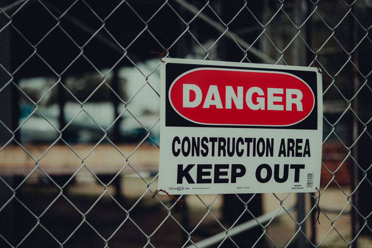 Close-up of a warning sign on a chain link fence at a construction site indicating danger.