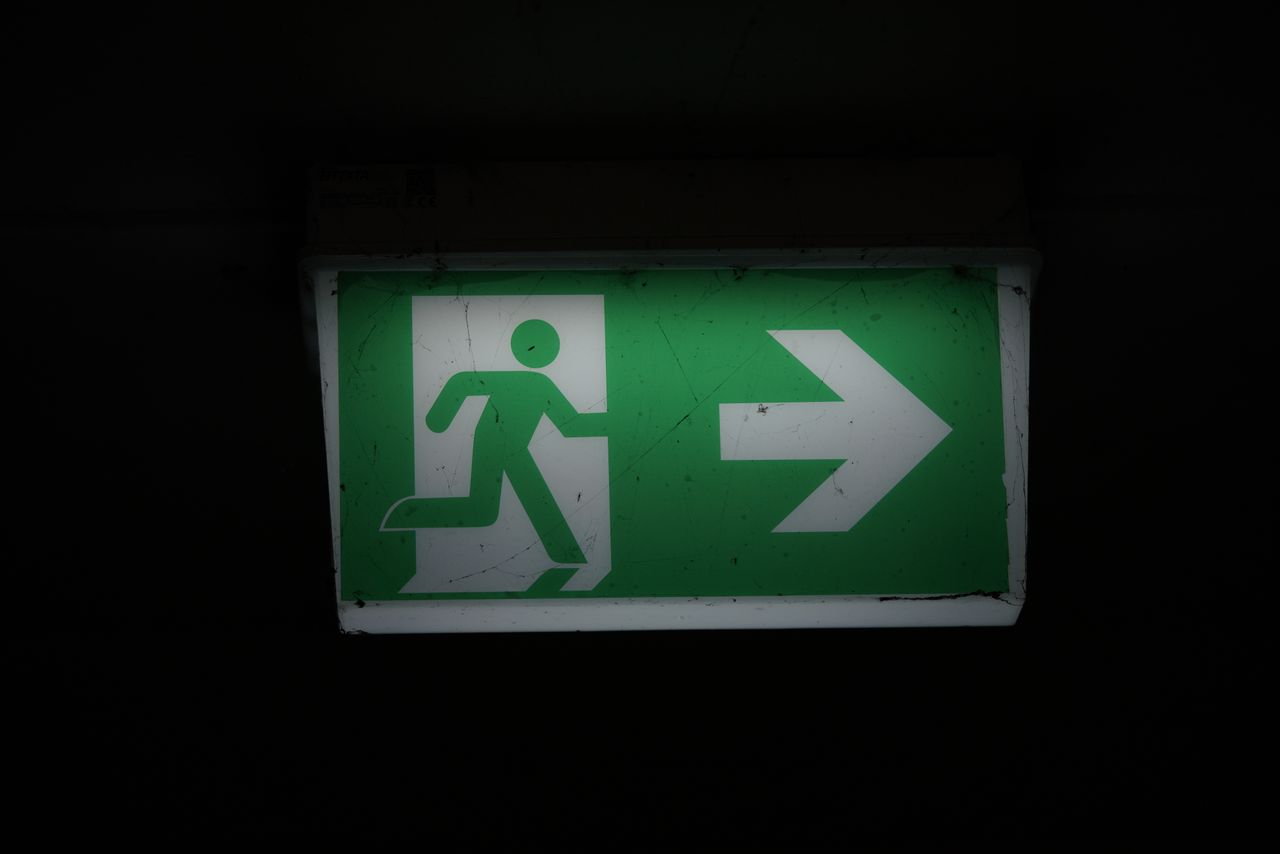 Illuminated green emergency exit sign with an arrow pointing right in a dark setting.